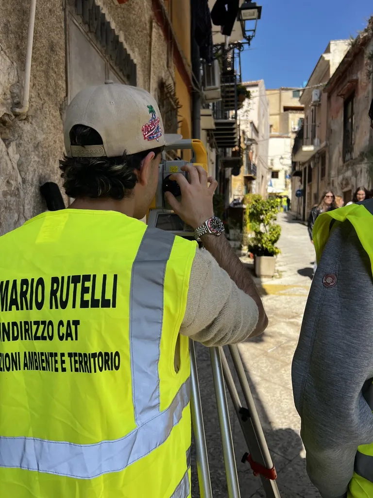 Studente dell'indirizzo CAT del Rutelli con gilet ad alta visibilità mentre esegue un rilievo con la stazione totale nel centro storico di Monreale.