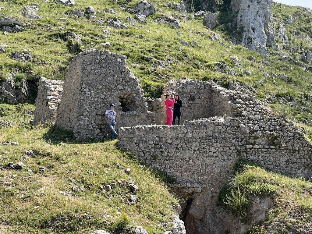 Due studentesse del CAT del Rutelli rilevano le mura della torre Sant'Anna con un ricevitore GNSS montato su palina, mentre l'insegnante tecnico-pratico osserva appoggiato alla parete