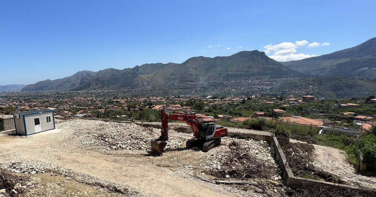 Il lotto di via Ignazio Florio a Monreale visto dalla strada, con una cabina di cantiere, un escavatore e i monti sullo sfondo
